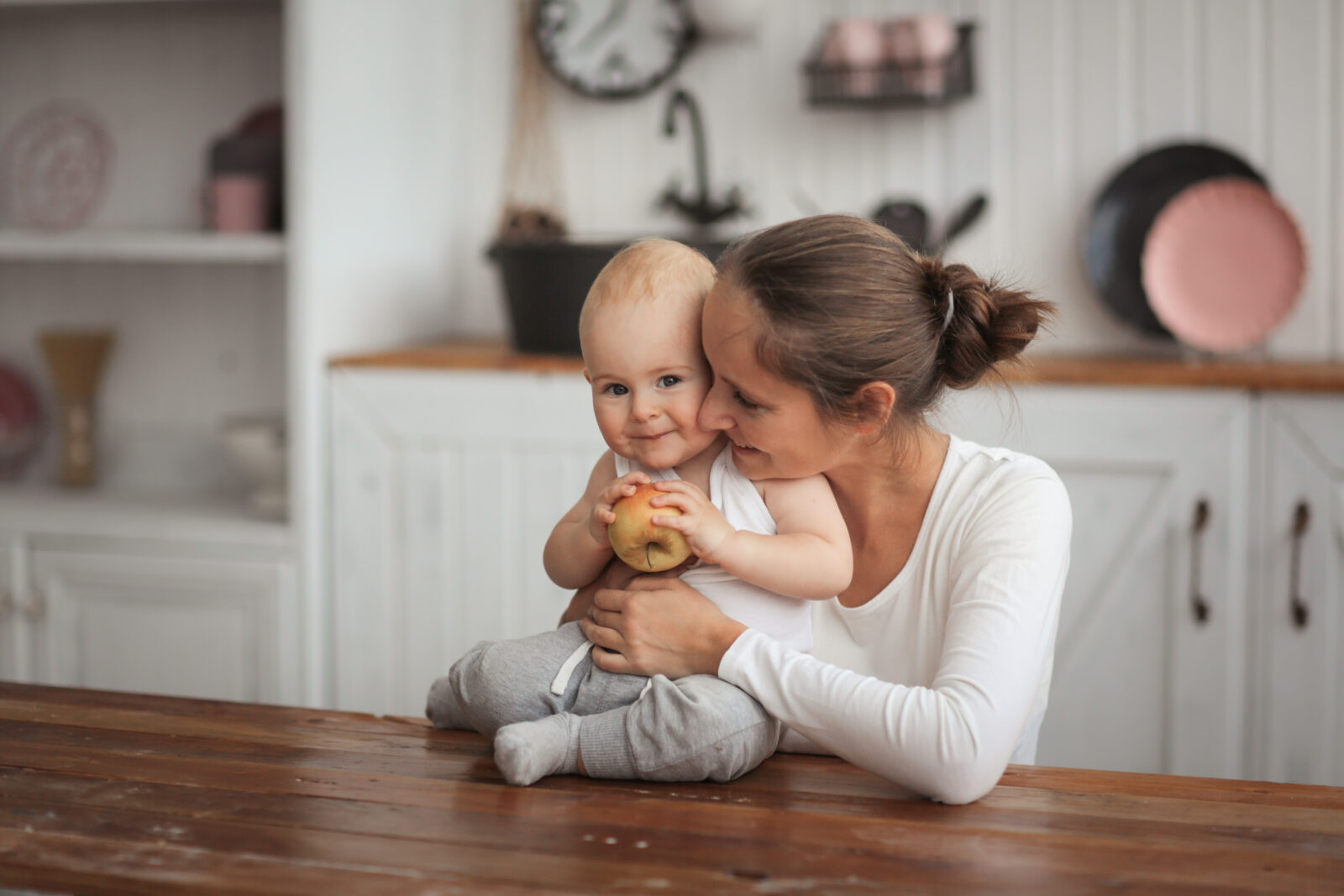Baby with an apple and caring mother in kitchen