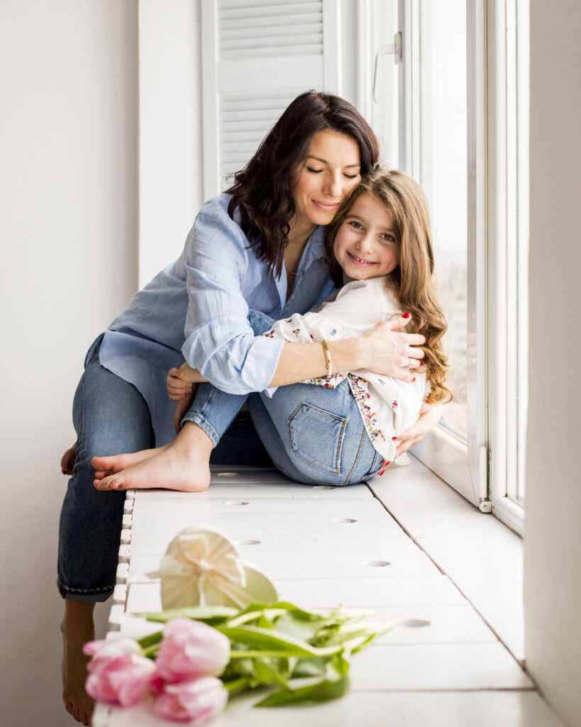 happy-mother-daughter-hugging-window-sill