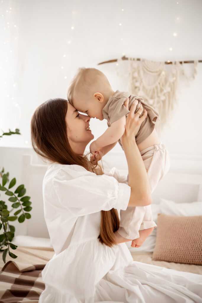a young beautiful mother with a baby boy hugging on the bed at home in the bedroom, mother's care and love, portrait of a happy mother with a child, healthy motherhood